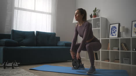 young-woman-is-training-buttocks-and-legs-squatting-with-weight-in-room-of-modern-apartment-bodybuilding-exercises-at-home-lady-in-sportswear